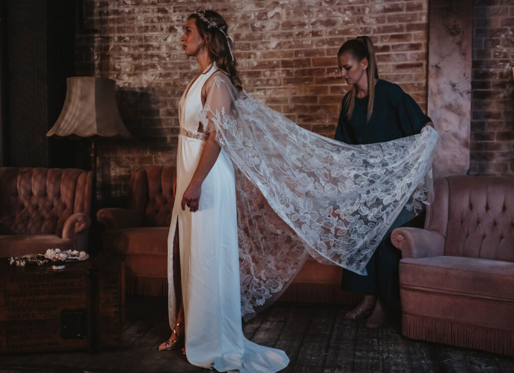 Brautstylistin hilft bei der Anprobe nach dem Braut Make-Up Brautstylistin hilft bei der Anprobe nach dem Braut Make-Up